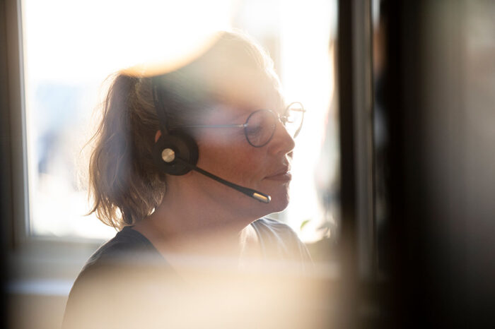 Woman with headset and glasses working at a computer, sunlight streaming through a window
